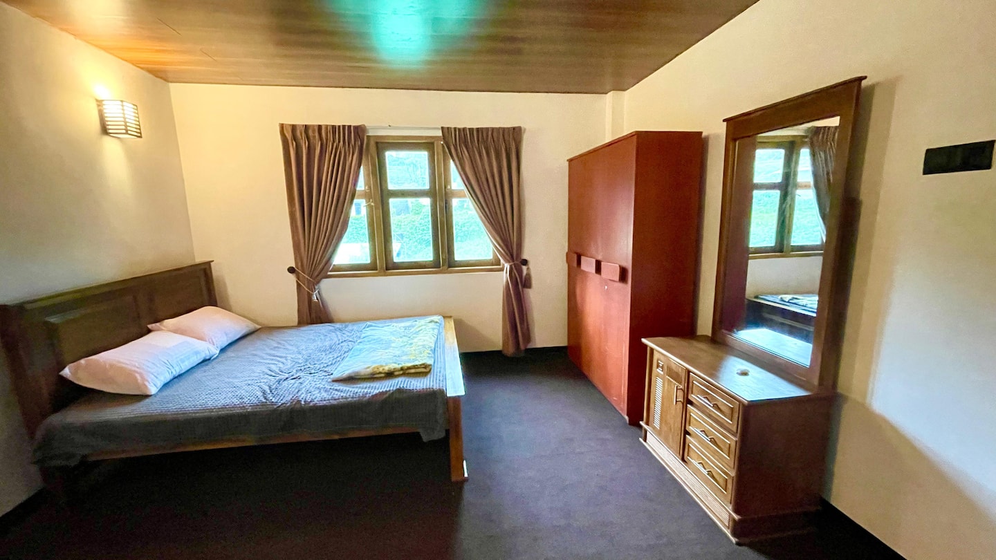 A carpeted bedroom with a double bed, wardrobe and window over the hills