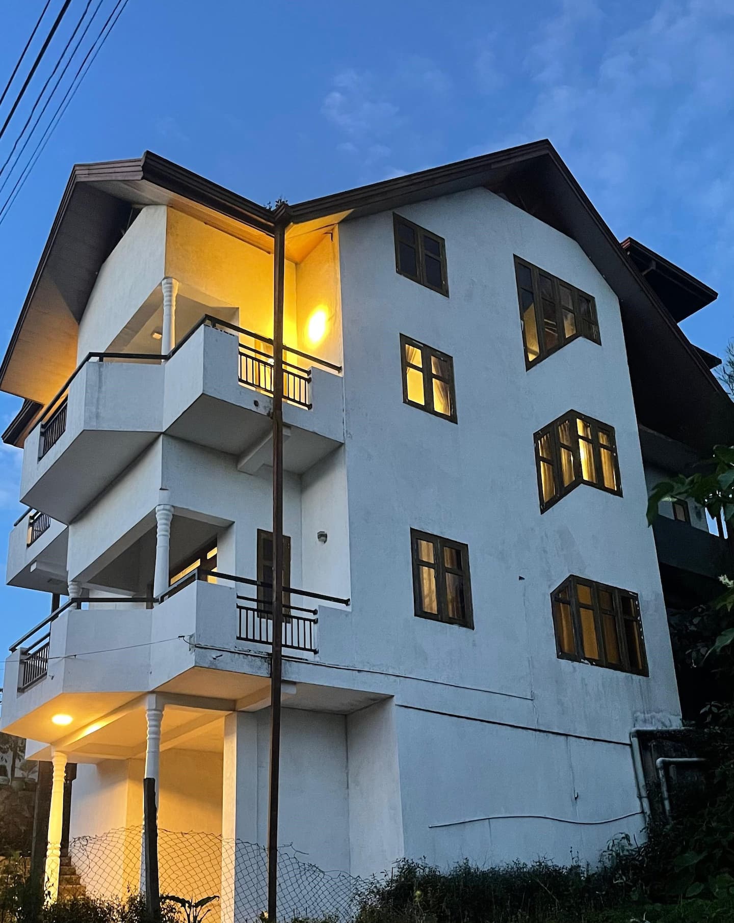 The whole guest house lit up at dusk, seen from the garden
